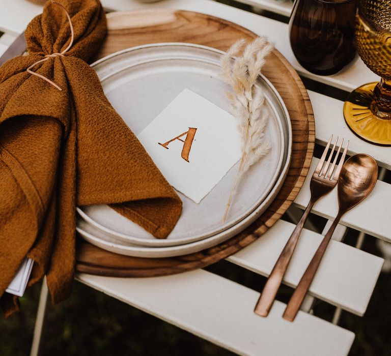 White plate with burnt orange napkin and sprig of pampas grass