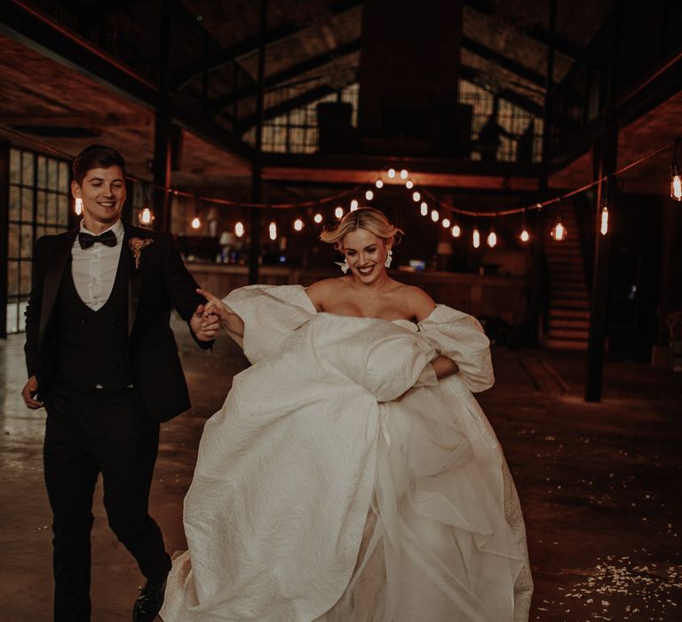 Bride in a stylish strapless wedding dress with blouson sleeves and dangly earrings running through the Hidden River Cabins wedding venue 