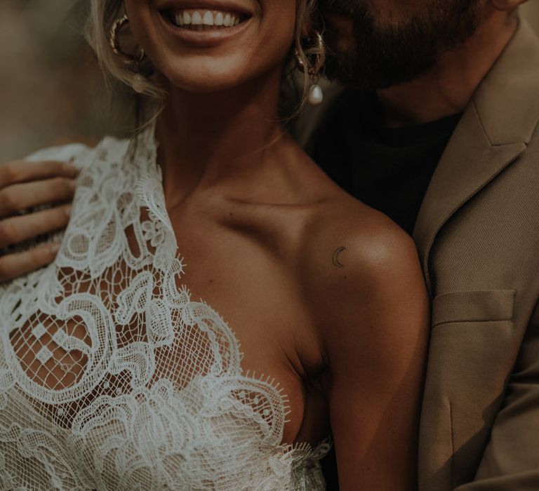 Smiling bride in a lace one shoulder wedding dress with pearl earrings