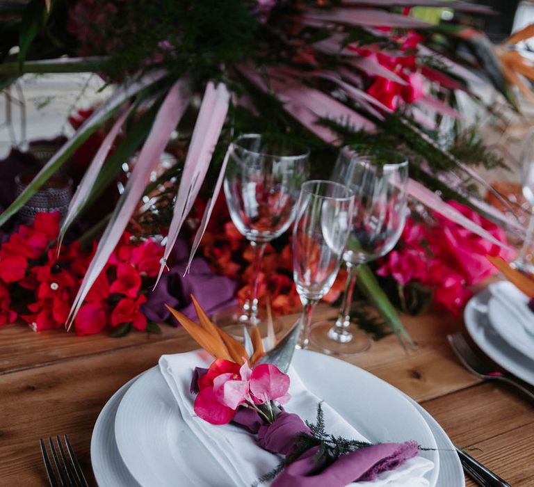 Pink faux flowers are tucked into a piece of purple fabric and sit on top of white plates and a white napkin. Photography by Stephanie Shenton. 