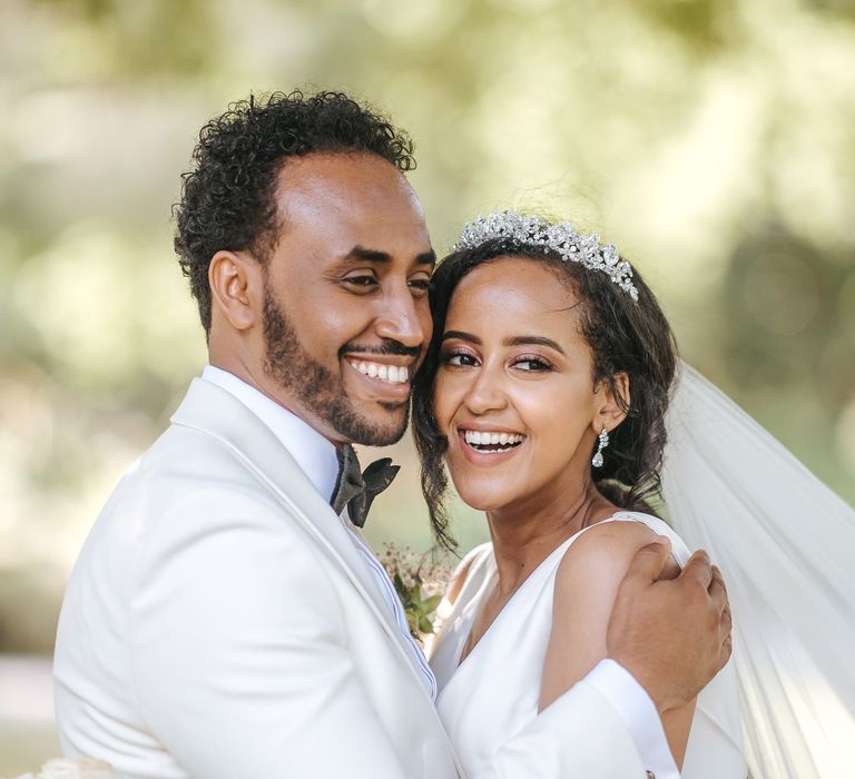 Intimate bride and groom portrait with groom in white tuxedo jacket and bride in a tiara 