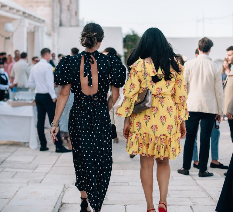 Stylish wedding guests wearing a black and white polka dot maxi dress with open back, and a short yellow floral dress