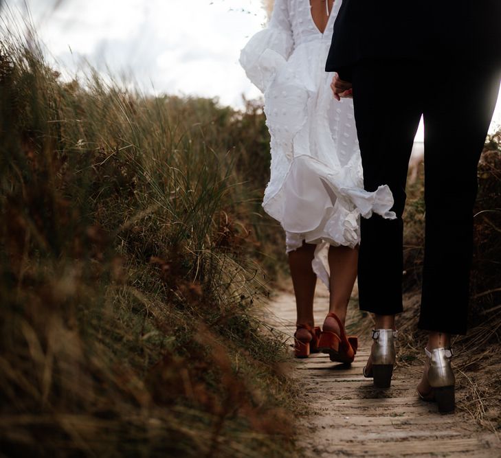 Two brides walk through beach dunes in block heels