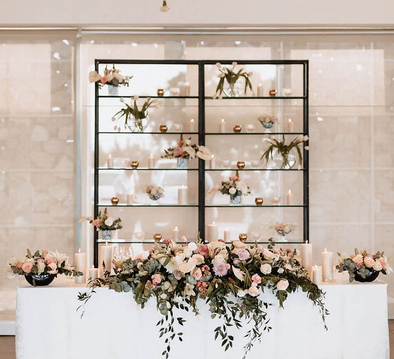 Sweetheart table with pink and white floral arrangement, pillar candles and hanging flower stems 