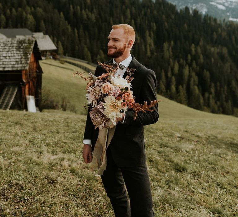 Groom holding an orange flower autumn wedding bouquet waiting for his bride to arrive