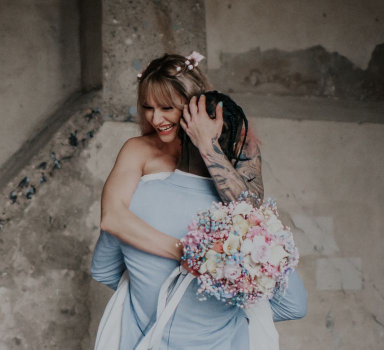 Groom in a blue suit picking up his bride with blue nail polish holding a pastel wedding bouquet 