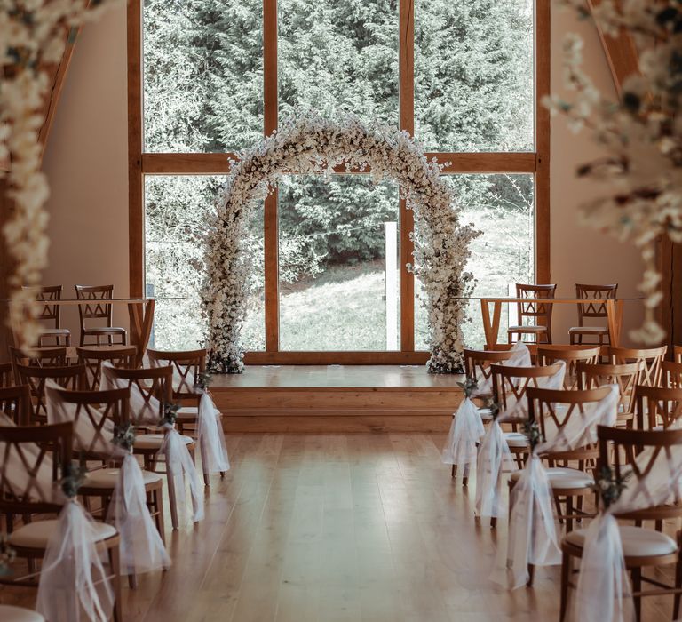 Wedding aisle lined with chairs and floral archway sits to the front of the room