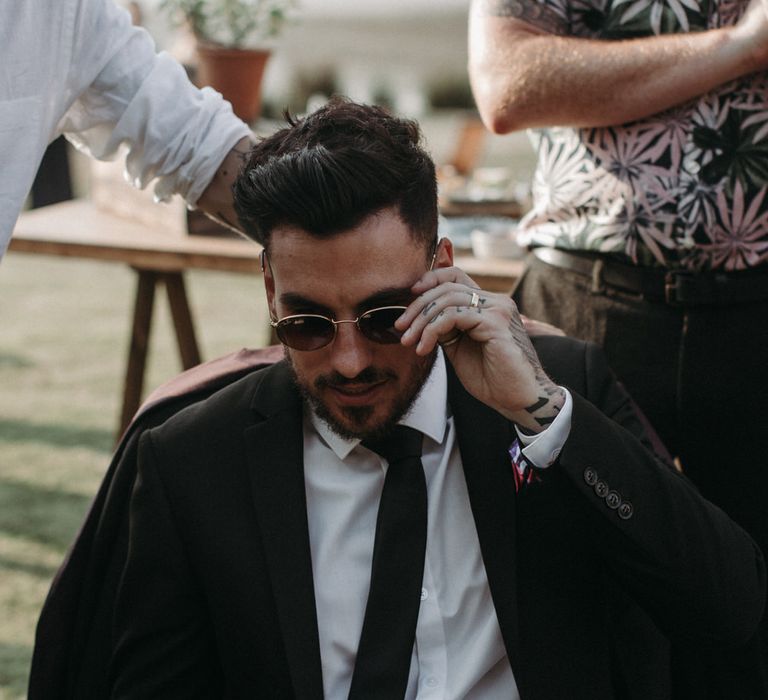 Groom wearing a black suit, Raybans and loafers for outdoor moody romantic wedding ceremony