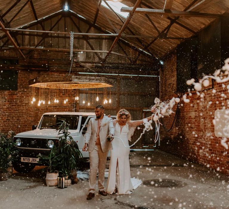 Bride and groom spraying champagne in a warehouse next to a large white 4x4 jeep with plants