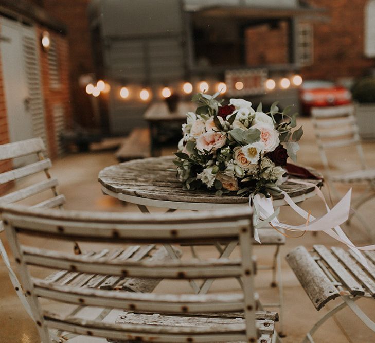 A bouquet of roses, brunia berries and eucalyptus lies on an outdoor bistro table.