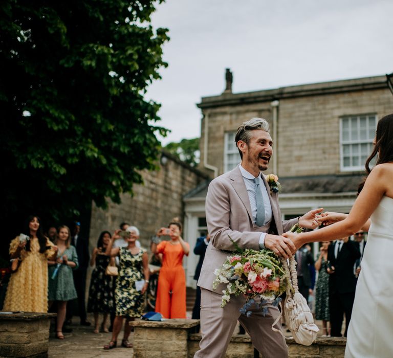 Bride in white strapless Rebecca Vallance Dress with bow detail at the back, veil and blue slingback heels holds multicoloured bouquet whilst dancing with groom in brown Moss Bros suit and blue tie in the courtyard at Hotel du Vin Harrogate after Harrogate wedding 