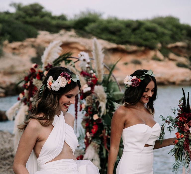 Two brides on the beach in Ibiza with floral headbands and a Jarlo London gown