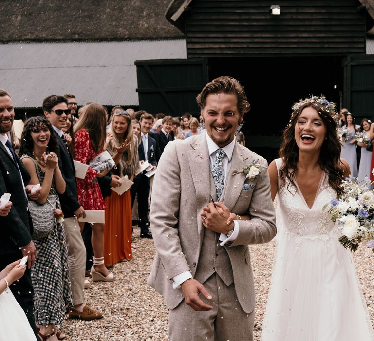 Bride & groom walk arm in arm together as confetti is thrown around them on their wedding day