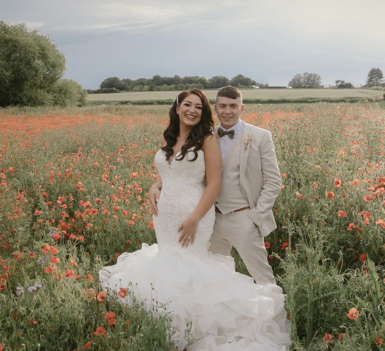 Bride and groom portrait in a poppy field with the bride in a Mori Lee mermaid wedding dress and groom in a three-piece beige suit