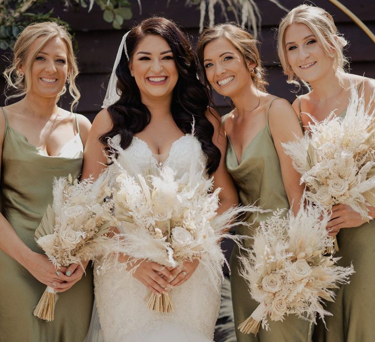 Bridal party portrait with bride in a lace fitted wedding dress and bridesmaids in green sating midi dresses 