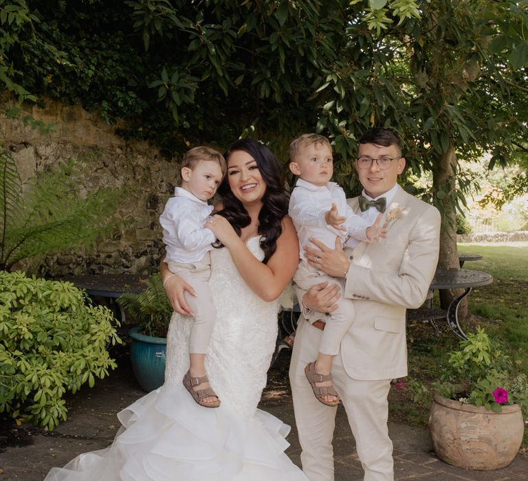 Bride and groom fairy portrait with their two boys. The bride wears a fishtail wedding dress and the groom and page boys beige suits 