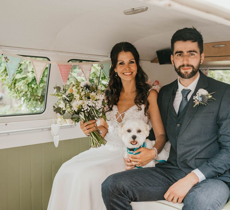 Bride & groom sit within vintage VW caravan as bride holds white floral bouquet