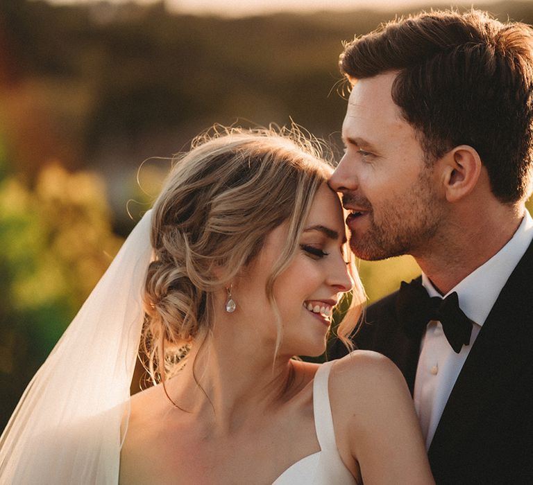 Golden hour bride and groom portrait with groom in a bow tie kissing his bride on the head 