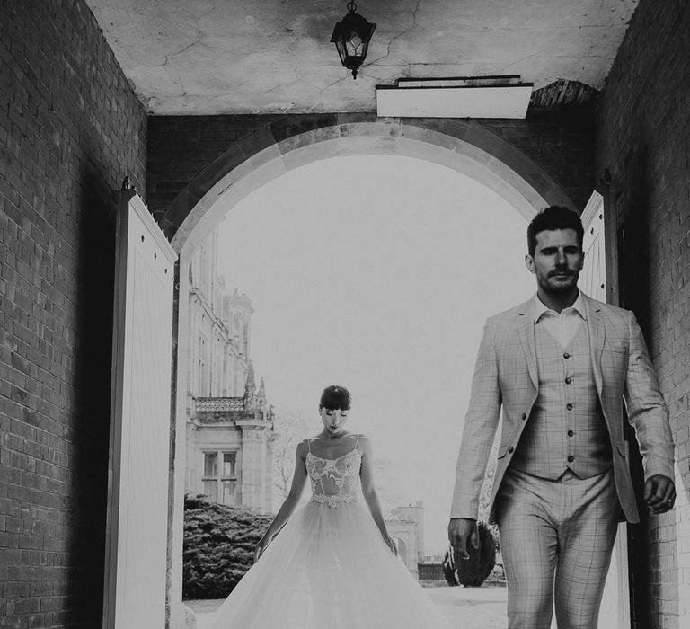 Black and white portrait of a groom in a check three-piece suit and bride in a tulle wedding dress with fitted bodice 