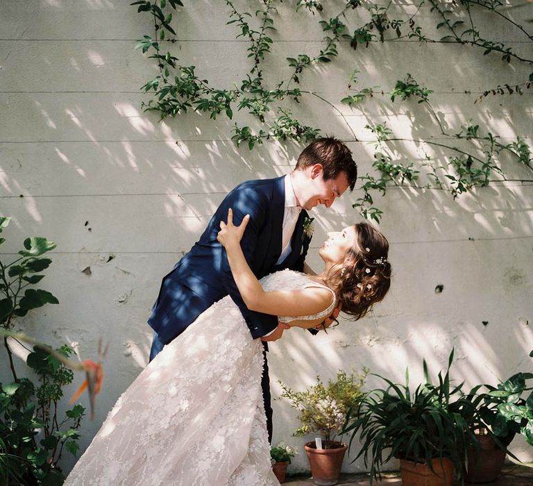 Groom dips his bride in front of vines as the sun shines through the trees 