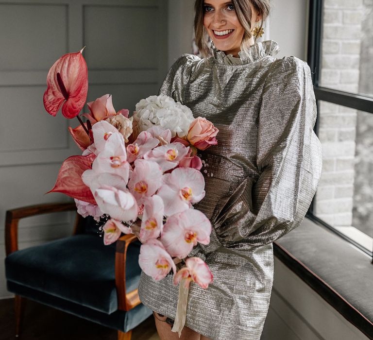 Bride in shiny gold short wedding dress with puff long sleeves and high detailed neck line with flower arrangements of small roses, large hydrangeas and orchids