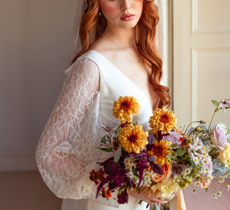 Bride with long curled hair, Juliet cap veil and long sleeve lace wedding dress holds multicoloured bridal bouquet