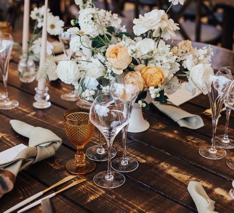 White and peach florals with amber glassware and gold cutlery at rustic wedding table for sperry tent wedding reception