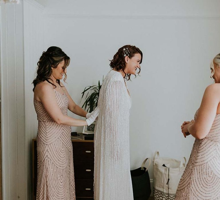 Bridesmaid does up brides wedding cape on the day of her wedding