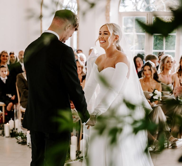 Beautiful bride with blonde hair tied back into a sleek ponytail wearing a strapless wedding dress with detachable long sleeves 