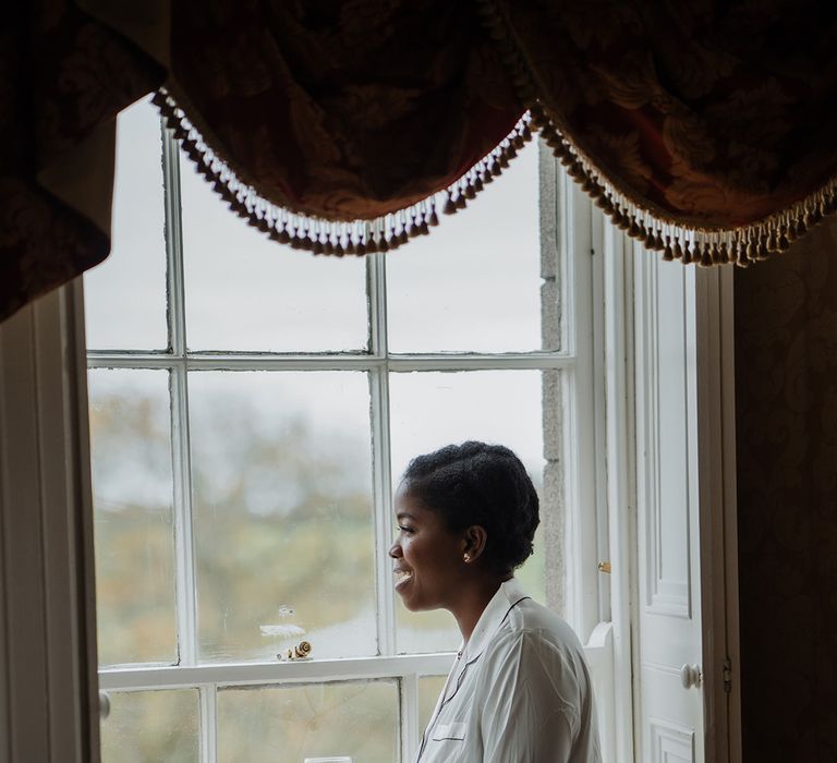 Black Bride smiles as she gets ready in silk white pajamas the morning of her wedding