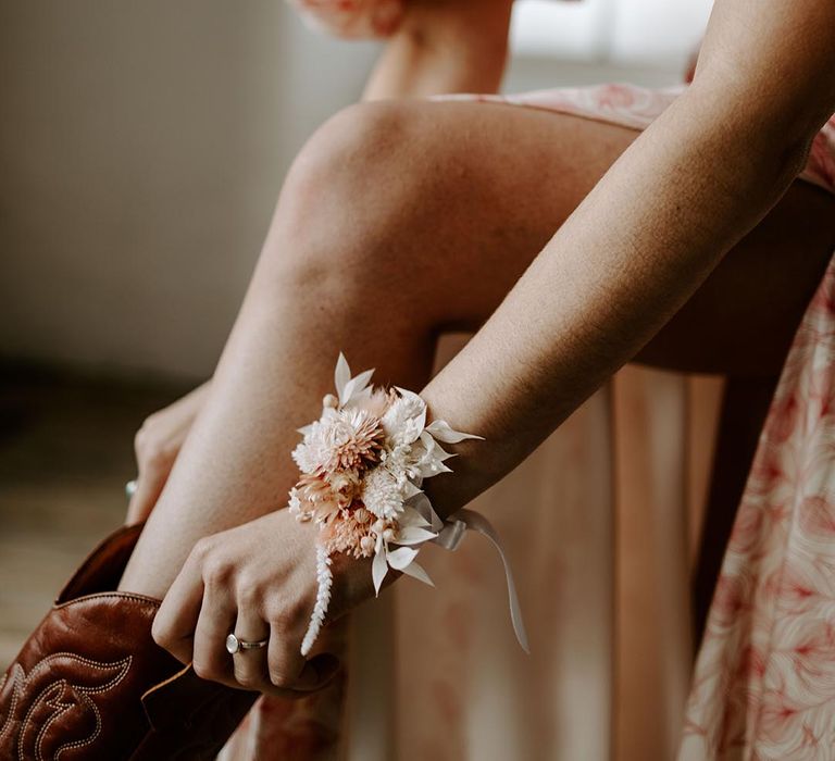 Boho bride in a pink print wedding dress, cowboy boots and a dry flower wrist corsage 