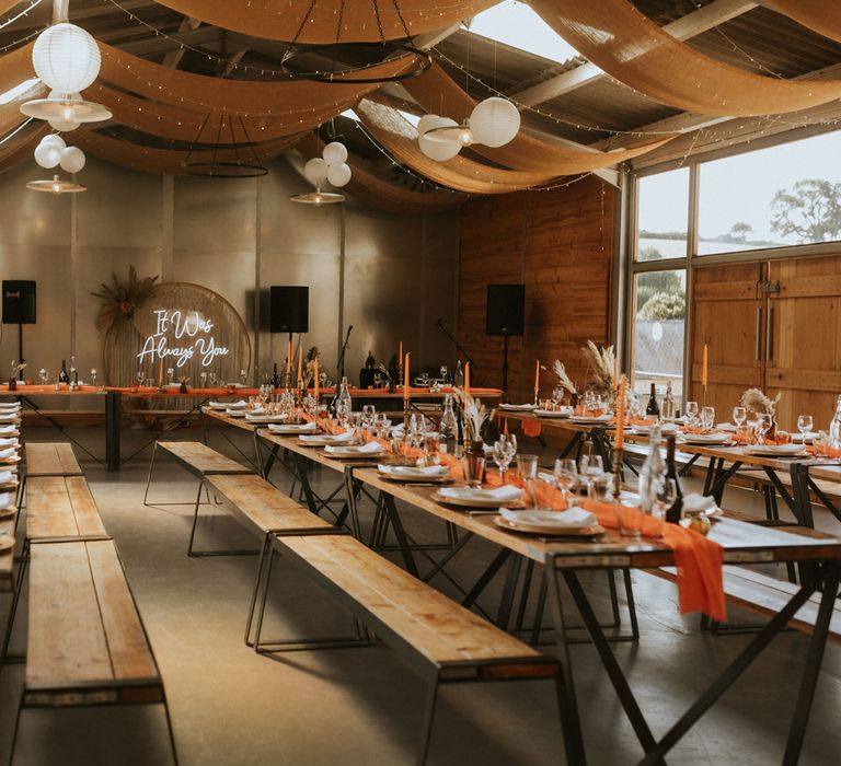 Modern rustic barn wedding reception with neon lights, orange draping and able runners and wooden tables