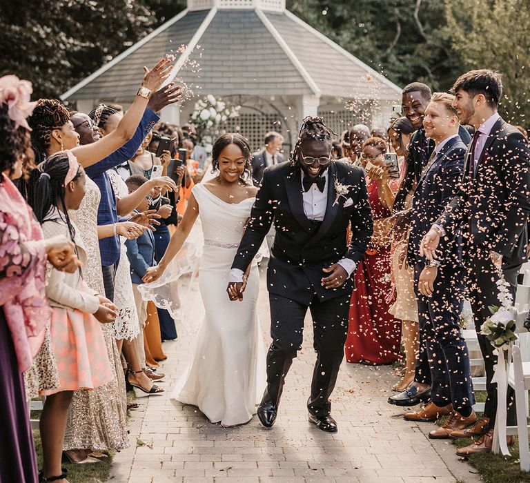 Bride & groom walk down the aisle as wedding guests throw confetti around them