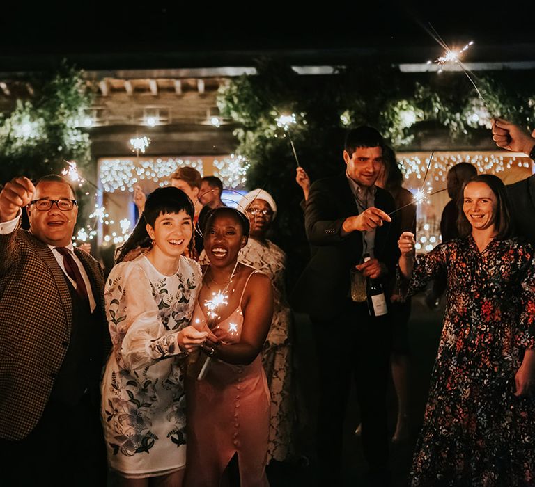 Sparkler moment with two brides in a pink satin midi dress and short embroidered dress 