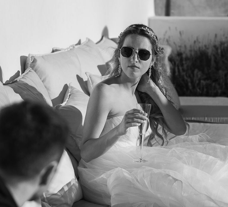 Bride wears sunglasses outdoors and holds champagne glass in black & white image