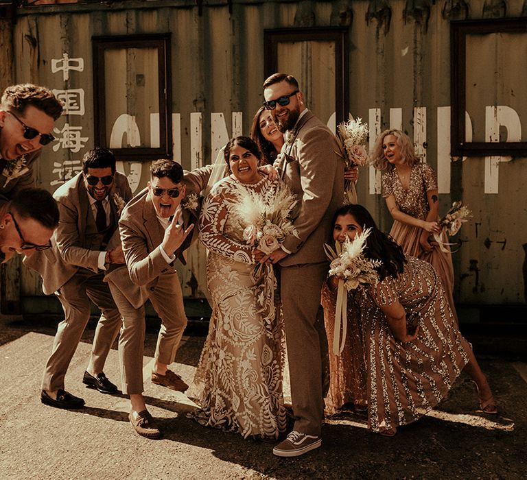 Fun wedding party photography at warehouse wedding with bride in a lace wedding dress, groomsmen in tweed suits and bridesmaids in tulle and sequin dresses 