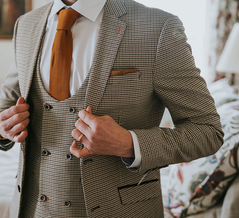 Groom in a dog tooth check three-piece suit with horseshoe waistcoat and orange waffle tie 