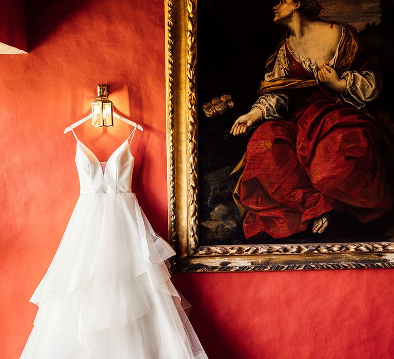 Lace and tulle wedding dress hangs from light fixture on red wall at Elmore Court wedding venue