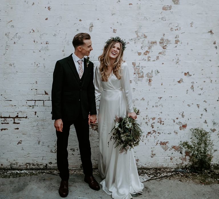 Bride & groom stand in front of white brick wall on their wedding day