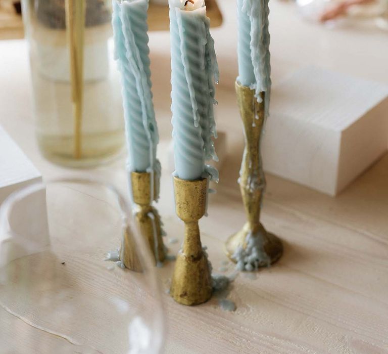 Twisted baby blue candles in golden candlestick holders as part of pastel theme for table settings