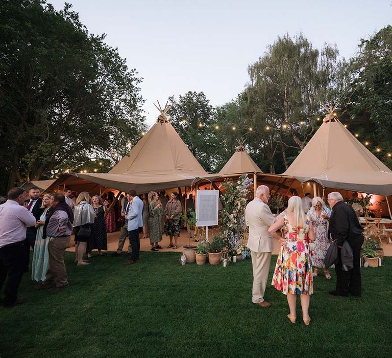 Wedding guests mingle outside of the beige Buffalo Tipi for garden wedding in Bath with fairy lights