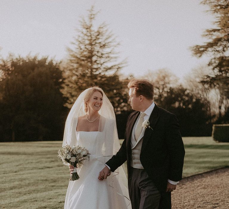 Bride in long white square neck long sleeved dress with full-length veil and groom at Hedsor House wedding