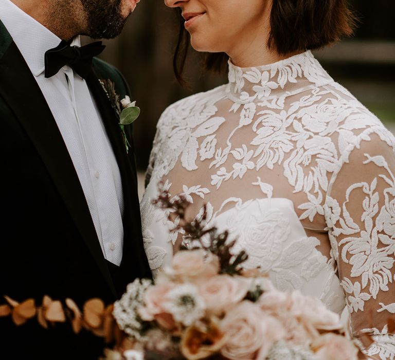 Bride with pearl hair accessory smiles as she rests her forehead against the groom's with matching buttonhole to the bouquet 