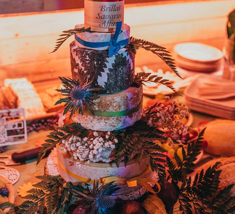 Cheese cake tower with wrapped cheeses and colourful ribbons decorated with foliage and fruits 