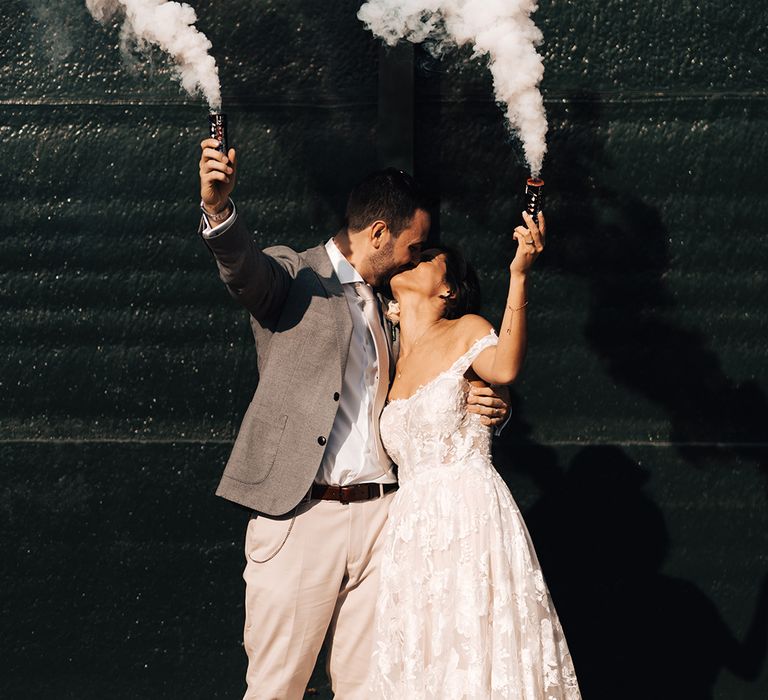 Bride and groom raise their smoke bombs as they share a kiss