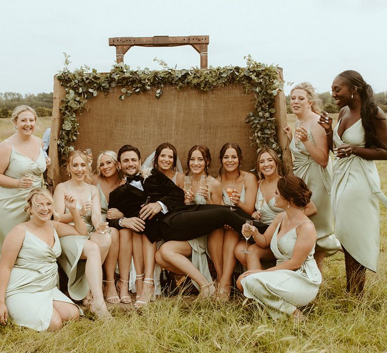 Bridal party and groom are seated and stood around back of the tractor decorated with foliage