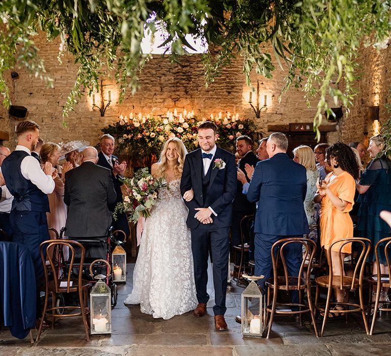 Bride and groom walk out of their ceremony as a married couple with lots of greenery decor 