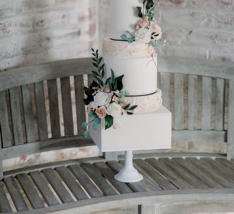 Four tier white iced wedding cake with flowers and foliage