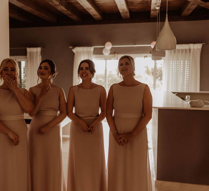 Bridesmaids wear matching pale pink dresses complete with cap sleeves as they see bride for the first time 