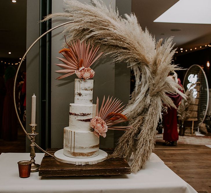 Three tier naked wedding cake featuring white frosting and complete with pink pastel decor and florals 